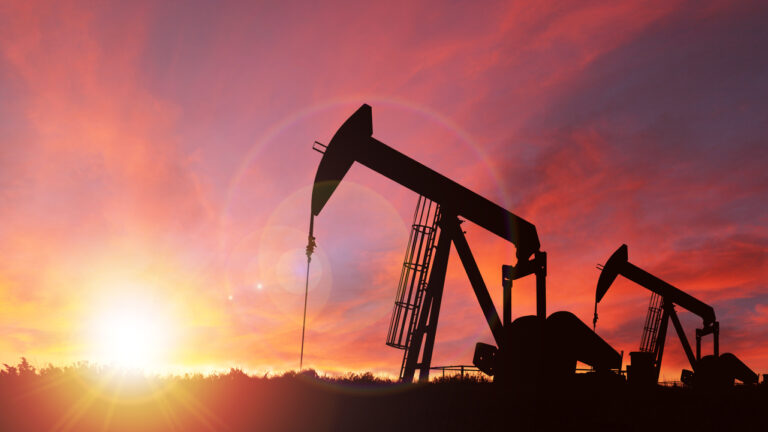 Pump jack silhouette against a sunset sky with deliberate lens flare and copy space. These jacks can extract between 5 to 40 litres of crude oil and water emulsion at each stroke.